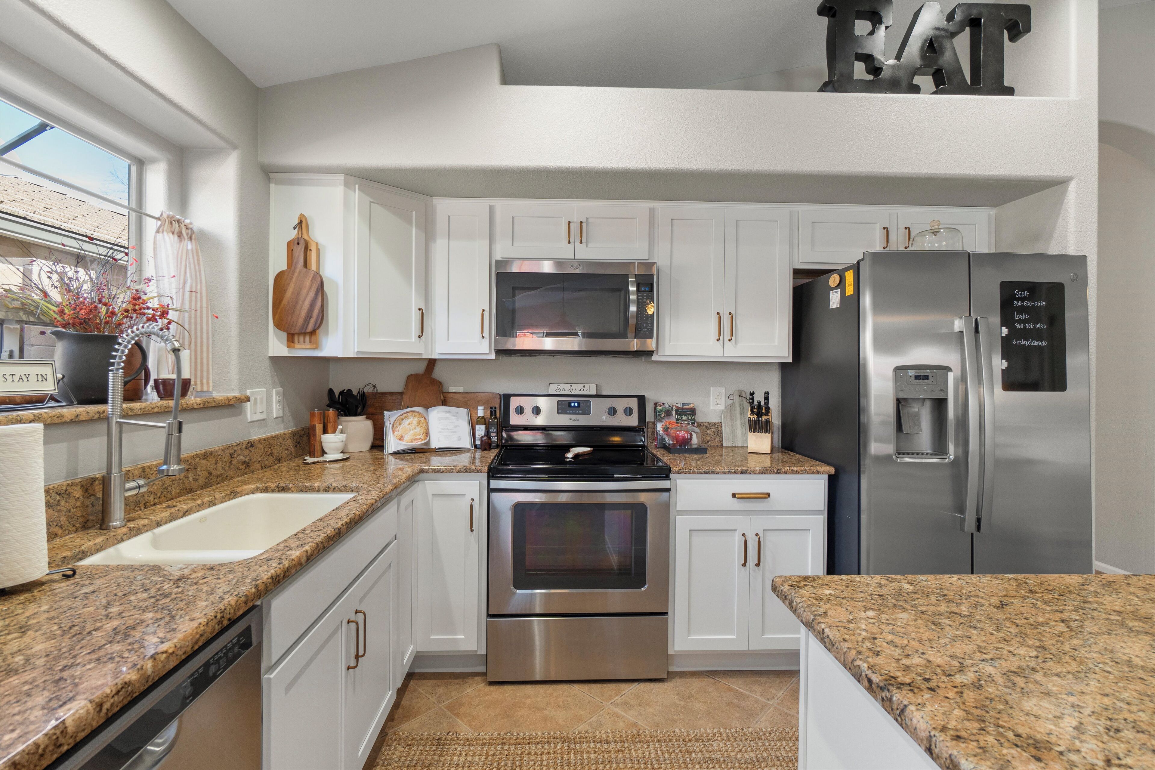 A modern kitchen with white cabinets, stainless steel appliances, granite countertops, and a window with a view.