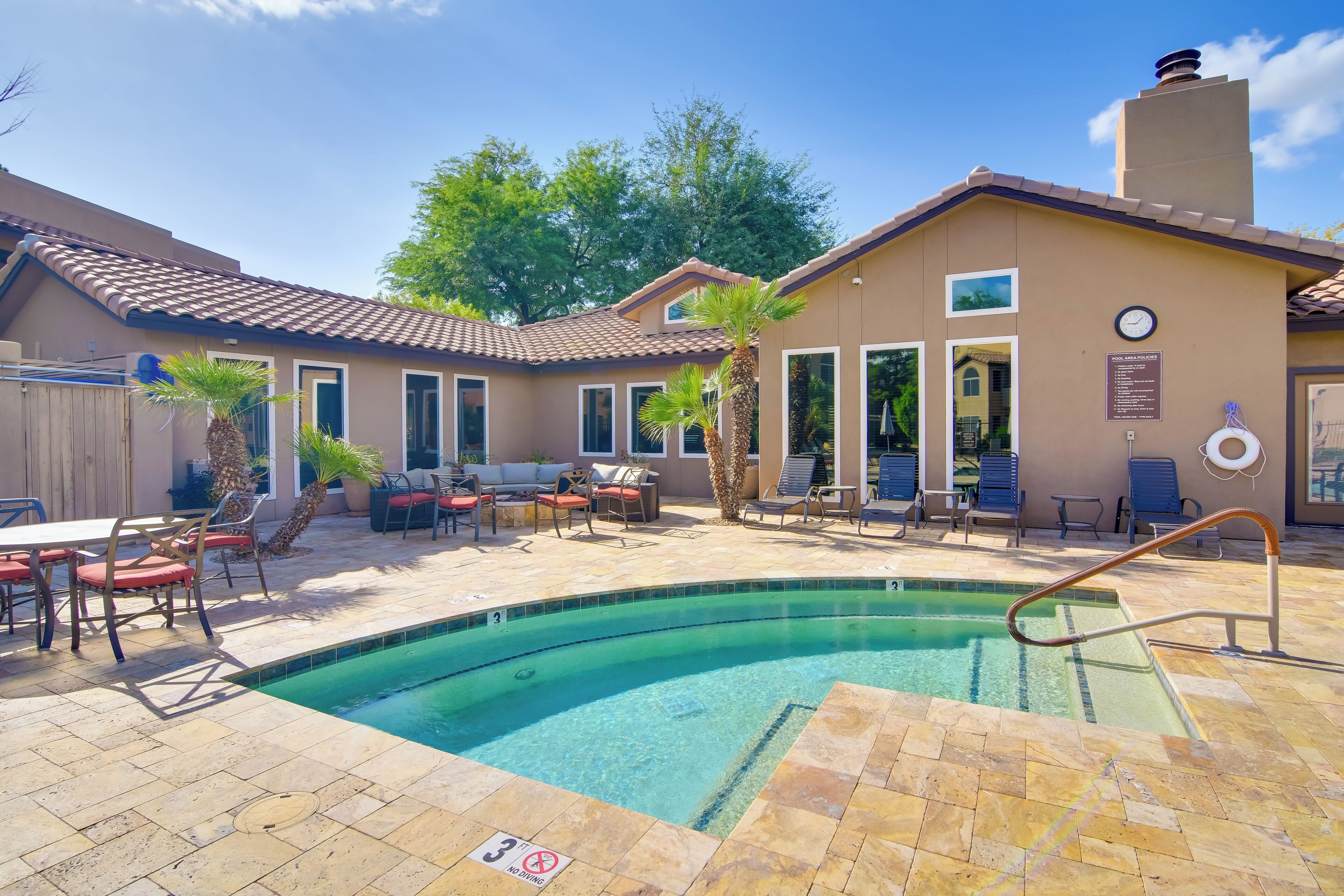 A swimming pool area with a patio, lounge chairs, and a covered seating area.