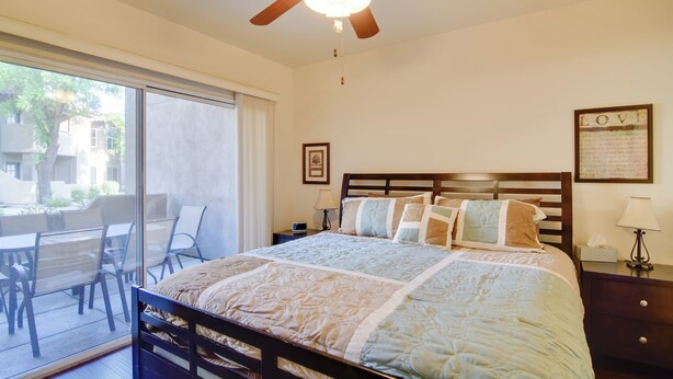A bedroom with a bed, a ceiling fan, a nightstand, a lamp, and a view of the outside. - Walkable Scottsdale Gem w/ Pool Access (Scottsdale)