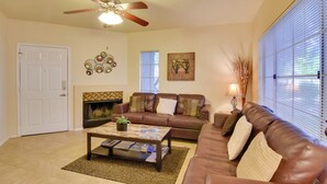 A living room with a brown leather sofa, a coffee table, a fireplace, and a ceiling fan. - Walkable Scottsdale Gem w/ Pool Access (Scottsdale)