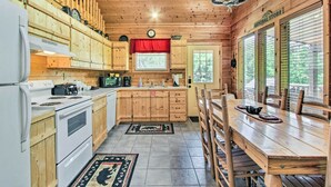A wooden cabin-style kitchen with a dining area, wooden cabinets, a stove, and a clock on the wall. - Cabin w/ Hot Tub & Deck ~ 12 Mi to Pigeon Forge! (Sevierville)