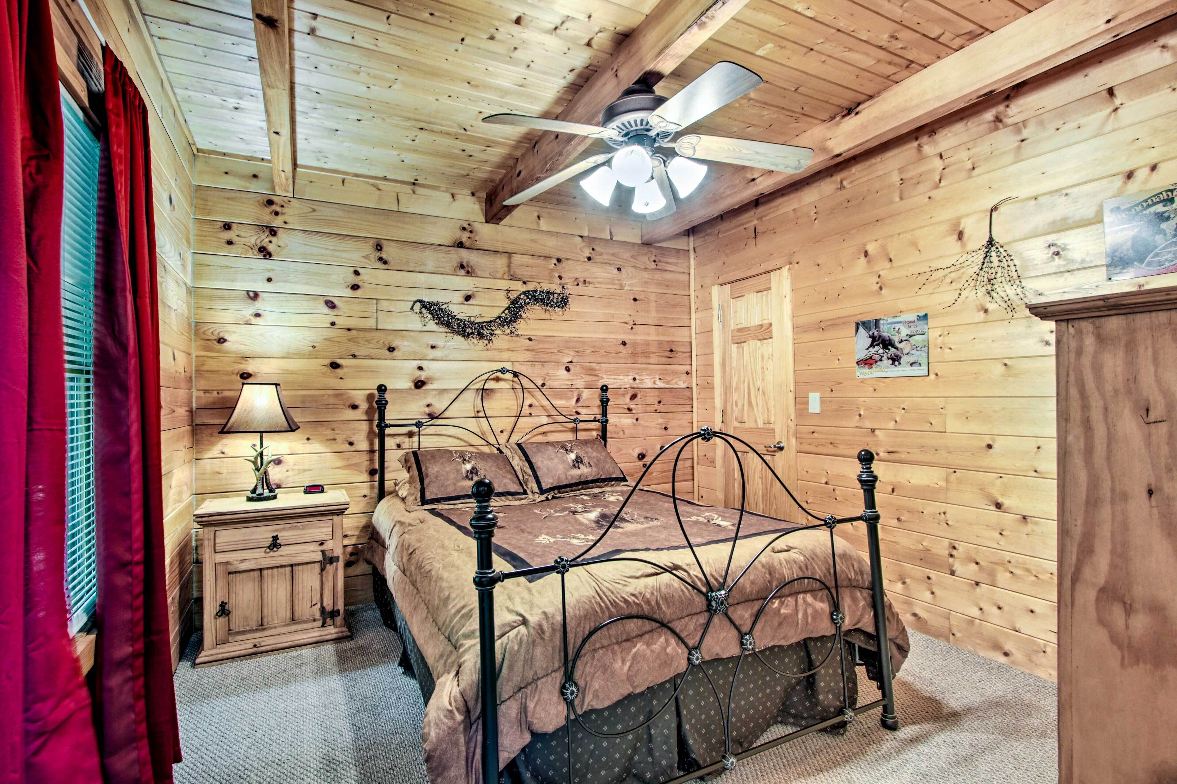 A wooden cabin bedroom with a bed, nightstand, lamp, ceiling fan, and a small wall decoration.