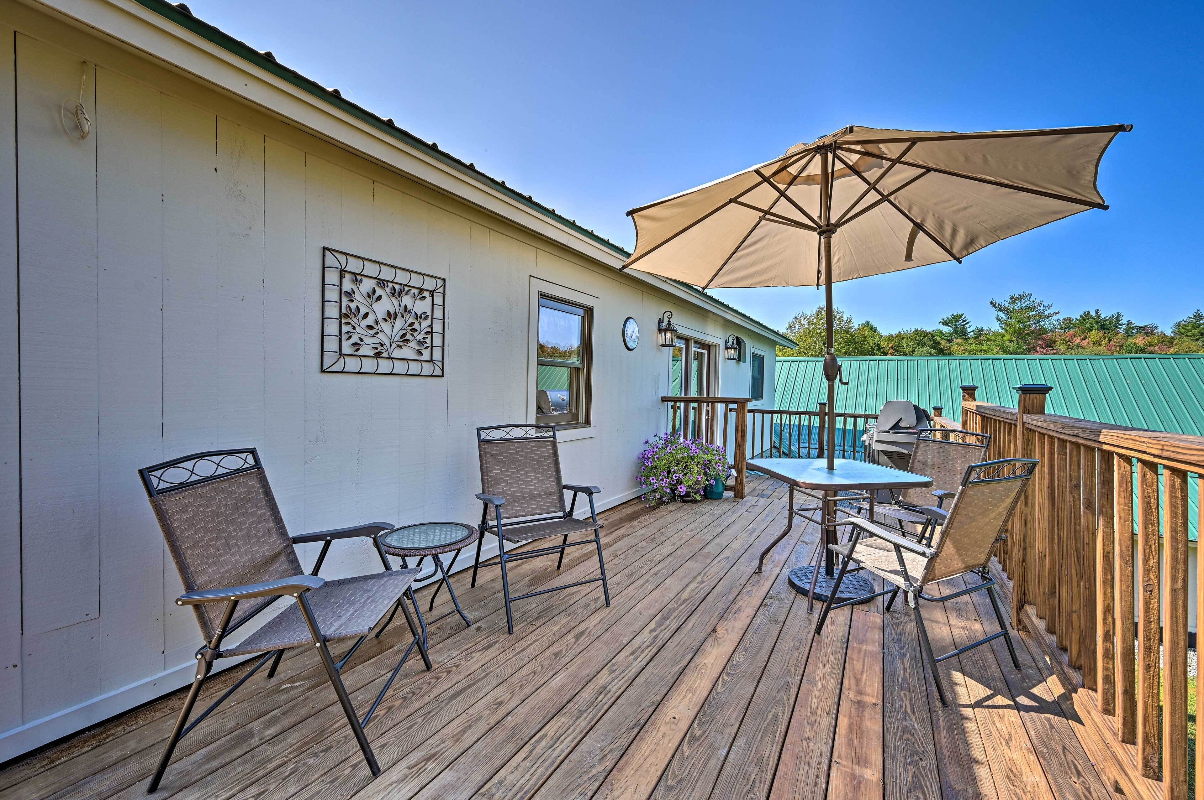 Eine Holzterrasse mit Gartenmöbeln, darunter Stühle und ein Tisch, sowie ein großer Sonnenschirm.
