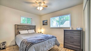 Une chambre à coucher avec un lit en bois, deux fenêtres, un ventilateur de plafond et une commode.