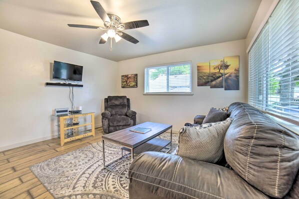 A living room with a ceiling fan, a flat-screen TV mounted on the wall, a leather sofa, a coffee table, and a patterned rug.