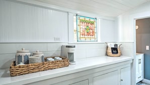 A kitchen with white cabinets, a coffee maker, and a wicker basket with jars.
