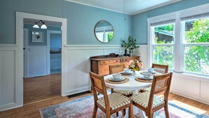 A dining area with a round table, wooden chairs, a white cabinet, and a large window with a view of greenery.