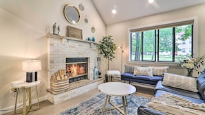 A living room with a fireplace, a sofa, a round table, and a large window with a view of trees. - Relax Fireside! Retreat 15 Mi to Camelback Slopes (Tobyhanna)