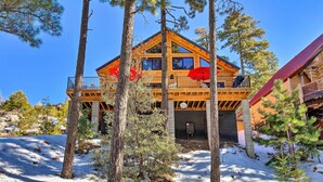 A two-story log cabin with a balcony and a red roof, surrounded by trees and snow. - Luxury Mountain Cabin w/ Furnished Deck + Views! (Mount Lemmon)