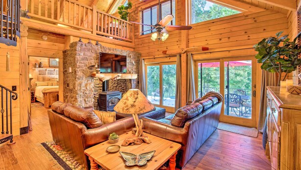 A spacious wooden cabin with a loft bedroom, a stone fireplace, leather sofas, and a dining area. - Luxury Mountain Cabin w/ Furnished Deck + Views! (Mount Lemmon)