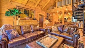A spacious living room with leather sofas, a coffee table, and a staircase leading to an upper level. - Luxury Mountain Cabin w/ Furnished Deck + Views! (Mount Lemmon)