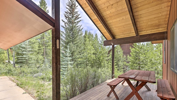 Una terraza de madera con mesas de picnic, rodeada de un bosque denso.