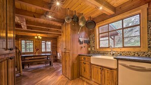 Interior de una cabaña de madera con cocina, que incluye armarios de madera, protector de salpicadura de piedra y un ventanal grande.