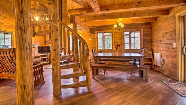 Interior de una cabaña de madera con una escalera espiral, un comedor y un televisor en la sala.