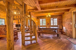 A wooden cabin interior with a spiral staircase, a dining area, and a television in the living room.