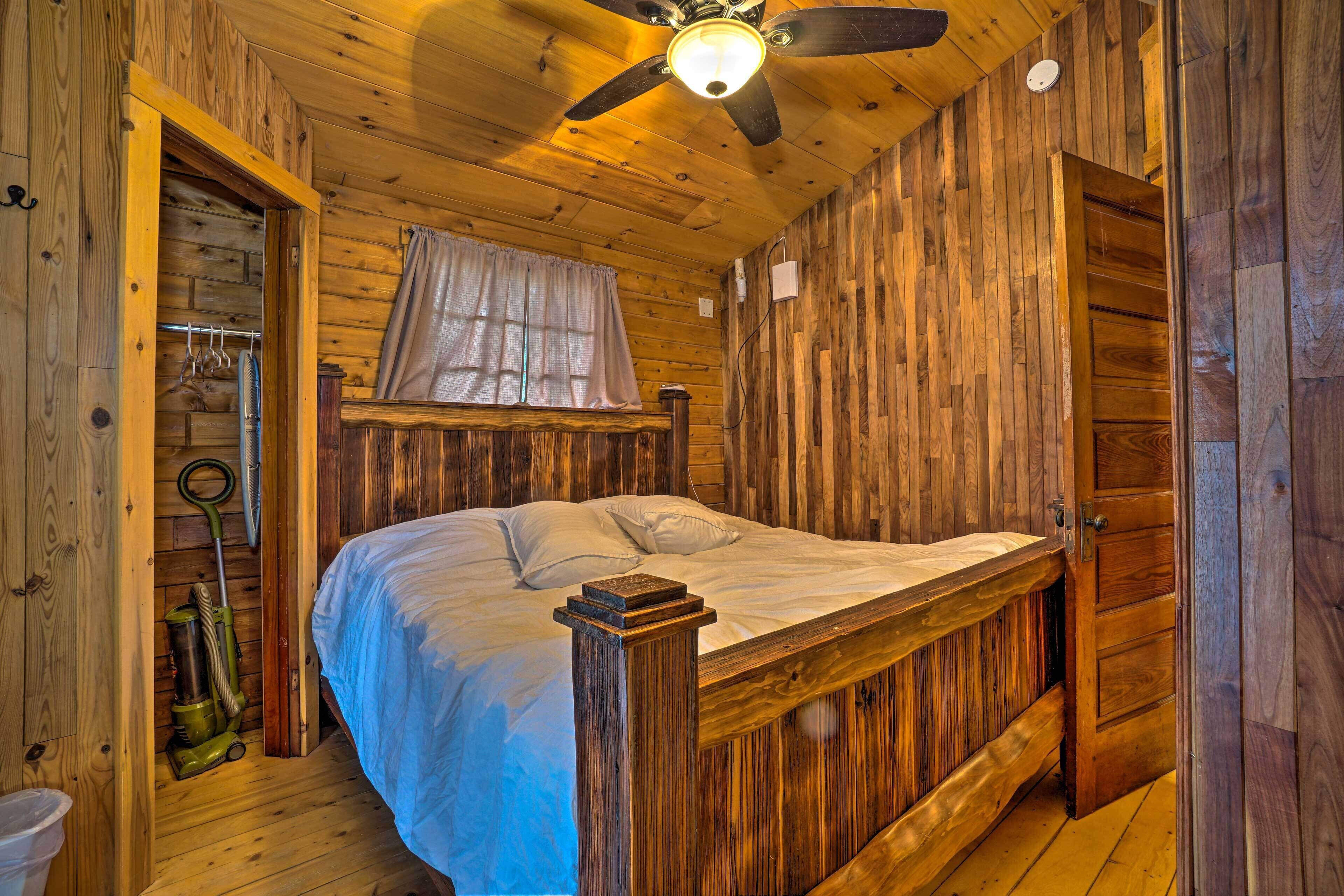 A wooden room with a bed, a ceiling fan, and a window with curtains.