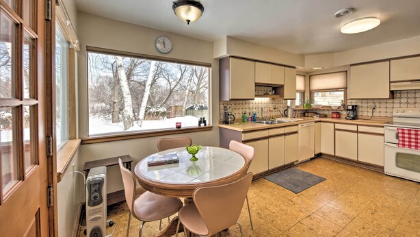 Una cocina con una mesa redonda, sillas, una ventana con vistas a árboles y un reloj en la pared.