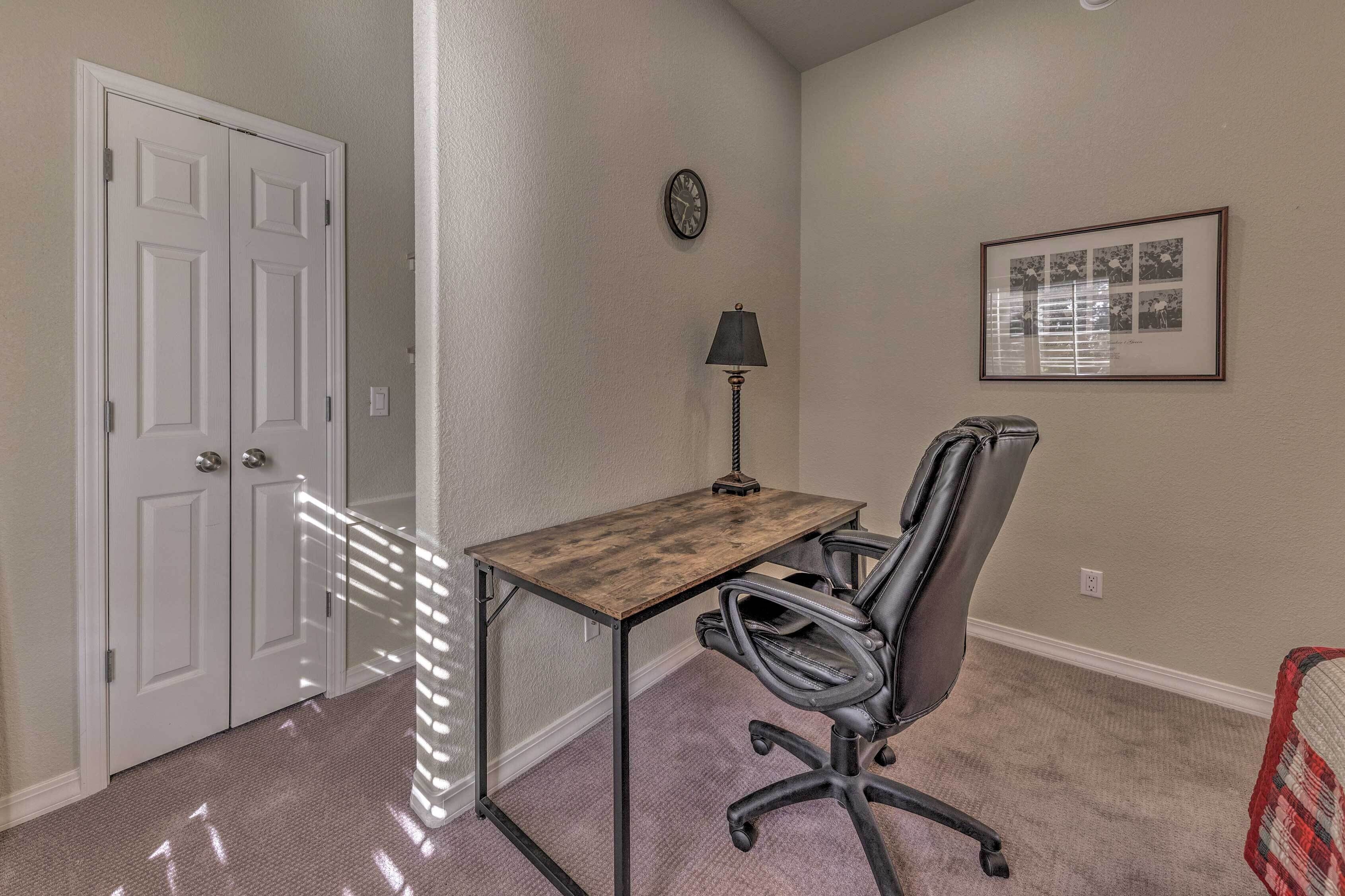 Une pièce comprenant un bureau, un fauteuil de bureau, une lampe, des tableaux encadrés et une porte.