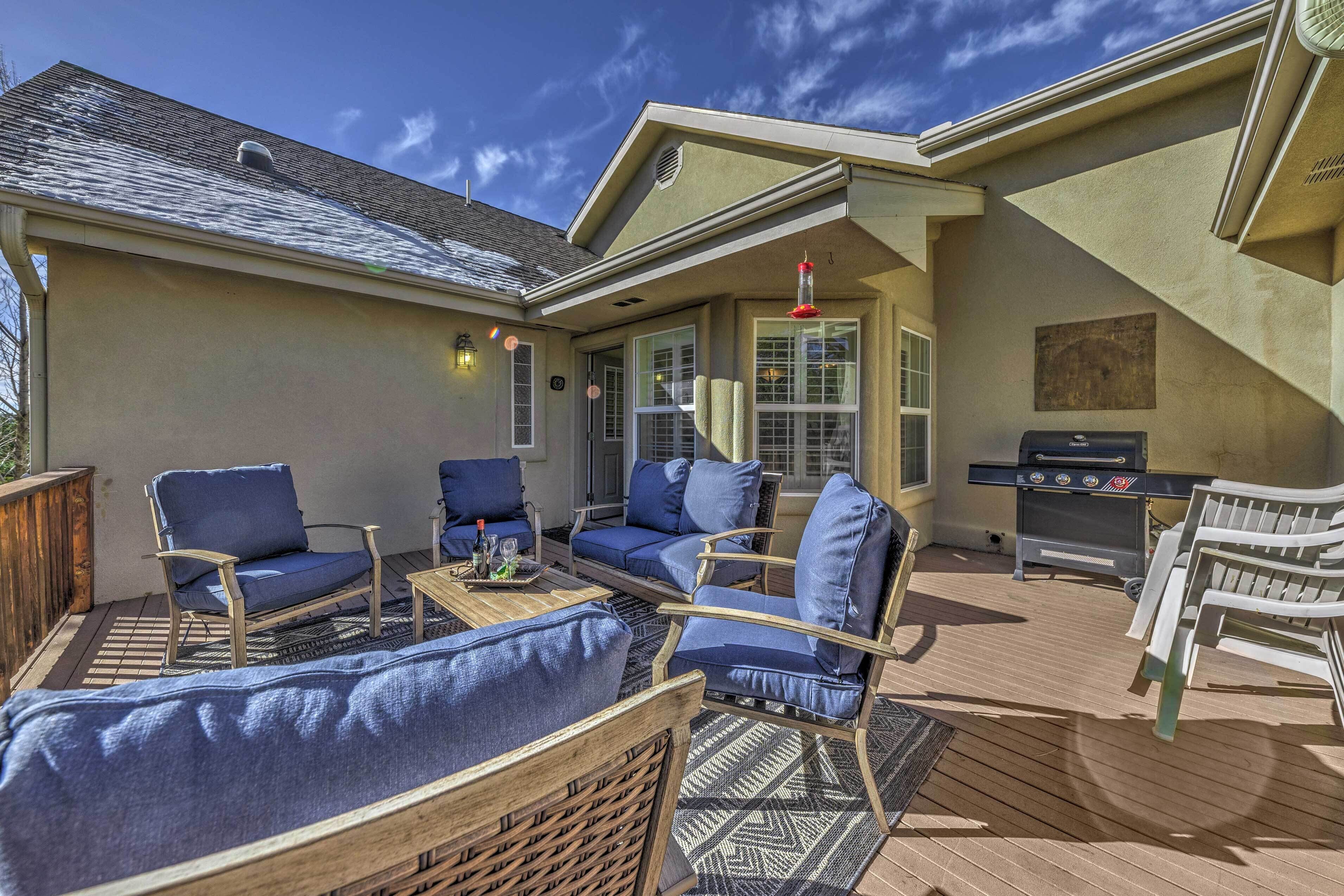 An outdoor patio with blue cushioned chairs, a wooden table, and a barbecue grill.
