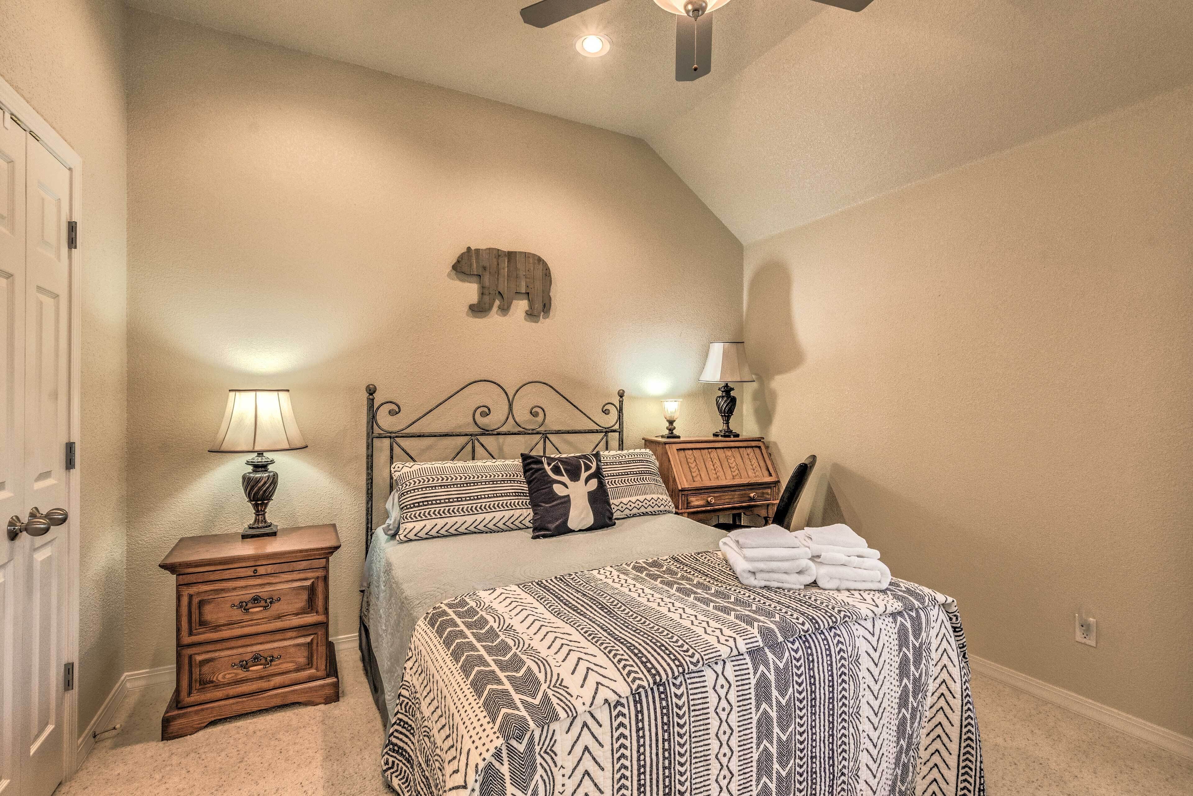 A bedroom with a bed, two bedside tables, a lamp, a wall-mounted bear decoration, and a ceiling fan.