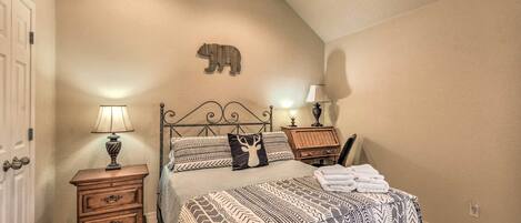 A bedroom with a bed, two bedside tables, a lamp, a wall-mounted bear decoration, and a ceiling fan.