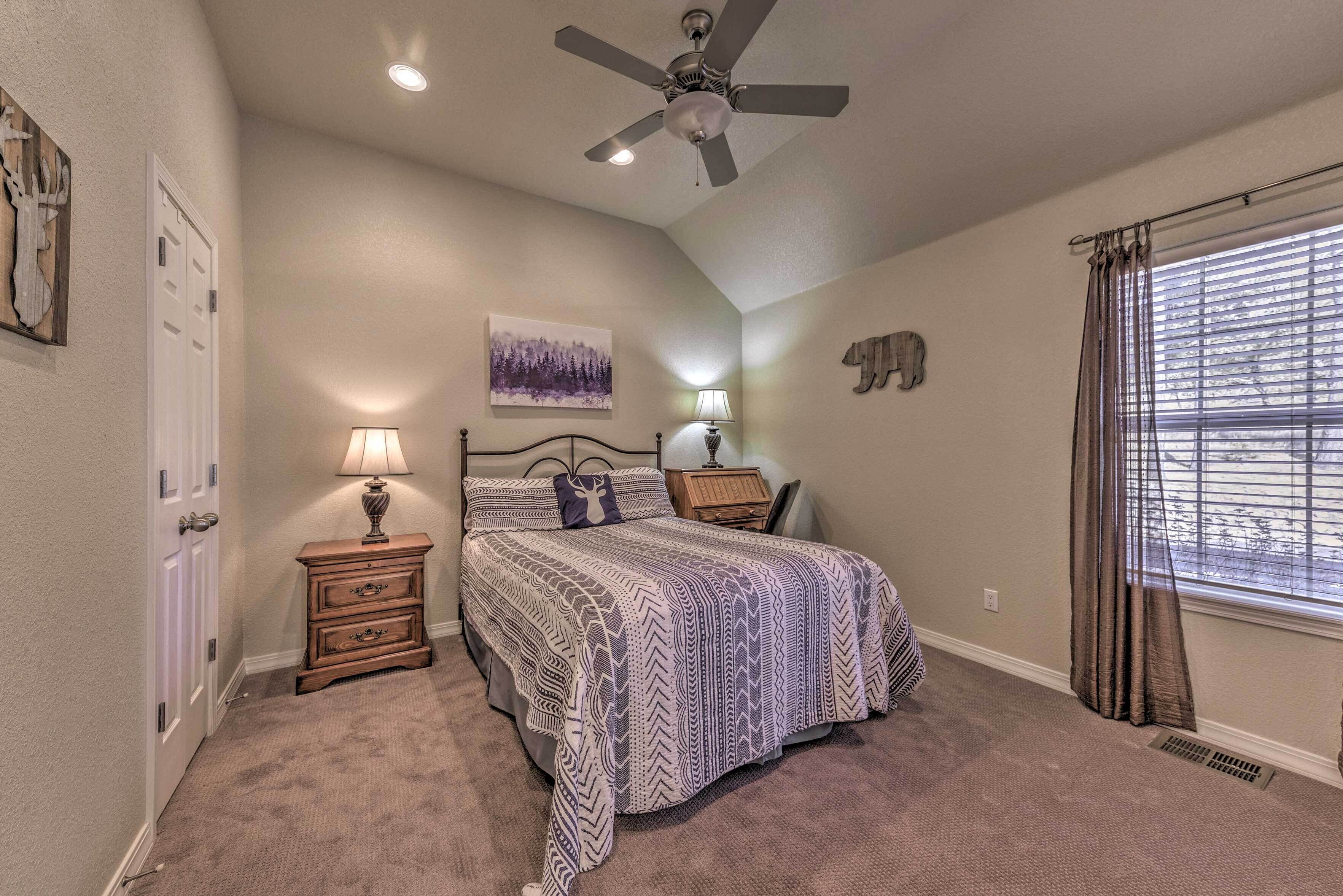 A bedroom with a bed, a ceiling fan, a nightstand with a lamp, a wall-mounted artwork, and a window with curtains.