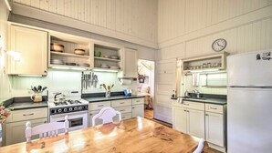 Cozinha com armários brancos, uma mesa de madeira e uma geladeira branca.