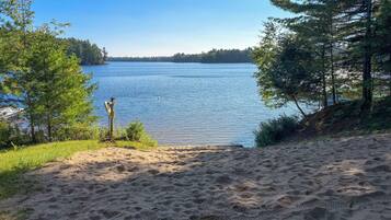 Una playa arenosa con un letrero de madera y una vista despejada de un lago rodeado de árboles.