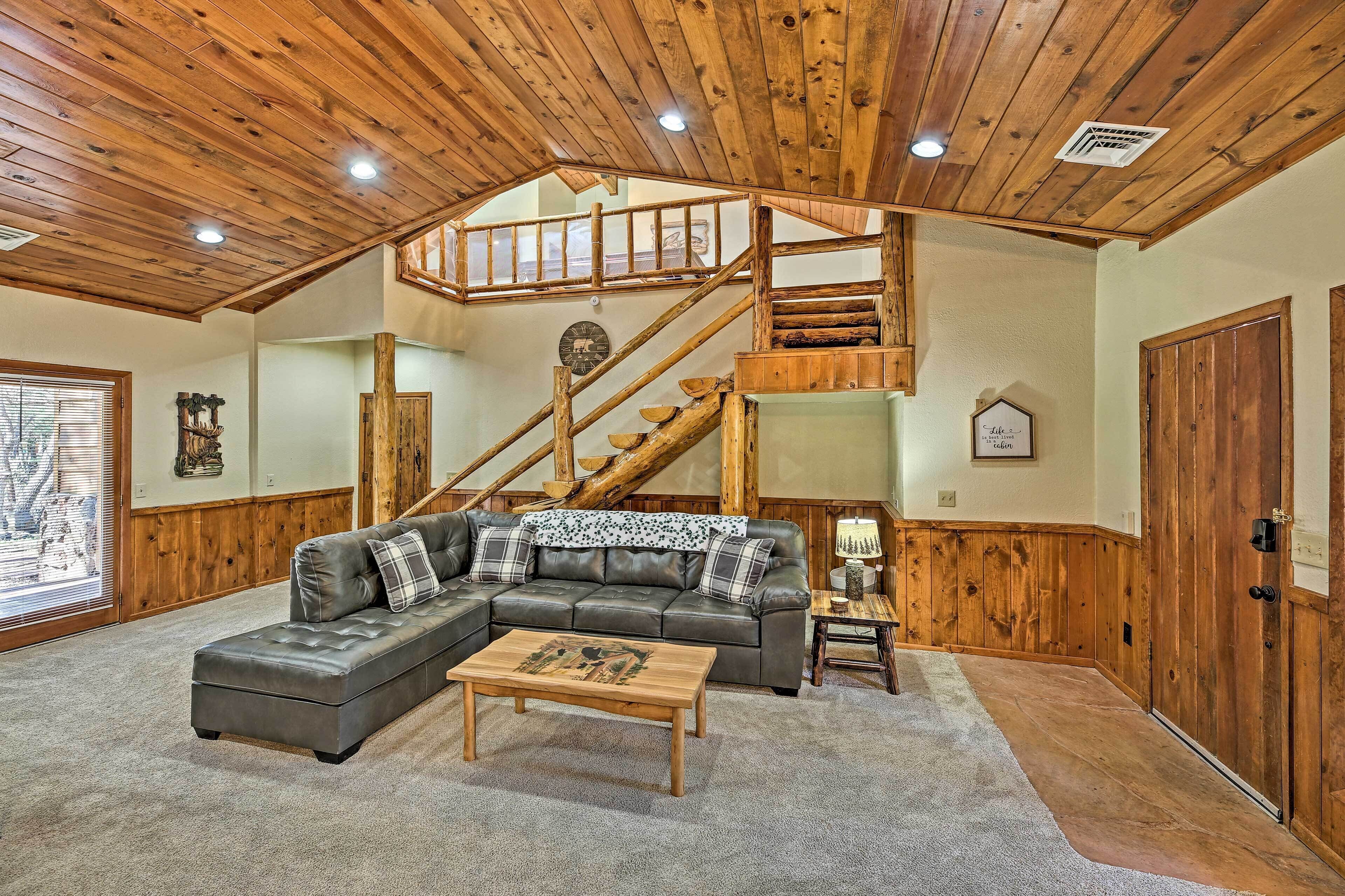Un salón amplio con un sofá seccional grande, una mesa de centro de madera y una escalera que conduce a un nivel superior.