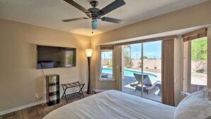 A hotel room with a large bed, ceiling fan, TV, and a view of a swimming pool.