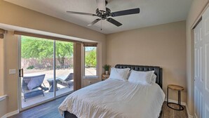 A bedroom with a large bed, a ceiling fan, a sliding glass door leading to an outdoor patio with chairs and a table, and a small round table next to the bed.