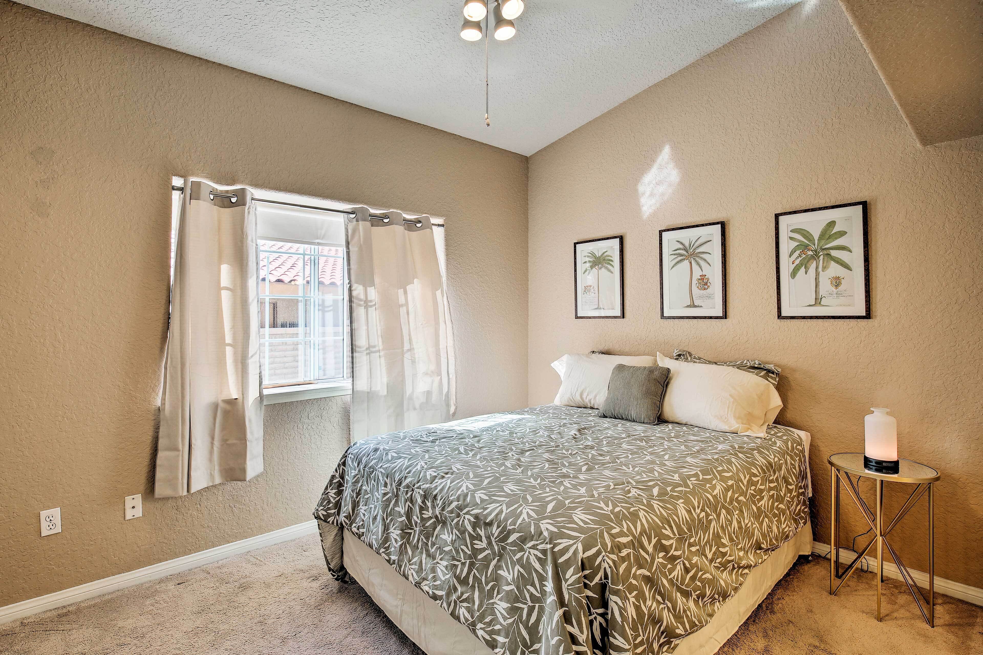 A bedroom with a bed, a bedside table with a candle, and three framed botanical prints on the wall.