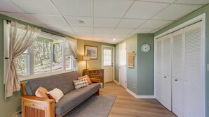 Un salon confortable avec un canapé, une lampe et une vue sur l’extérieur grâce à de grandes fenêtres.