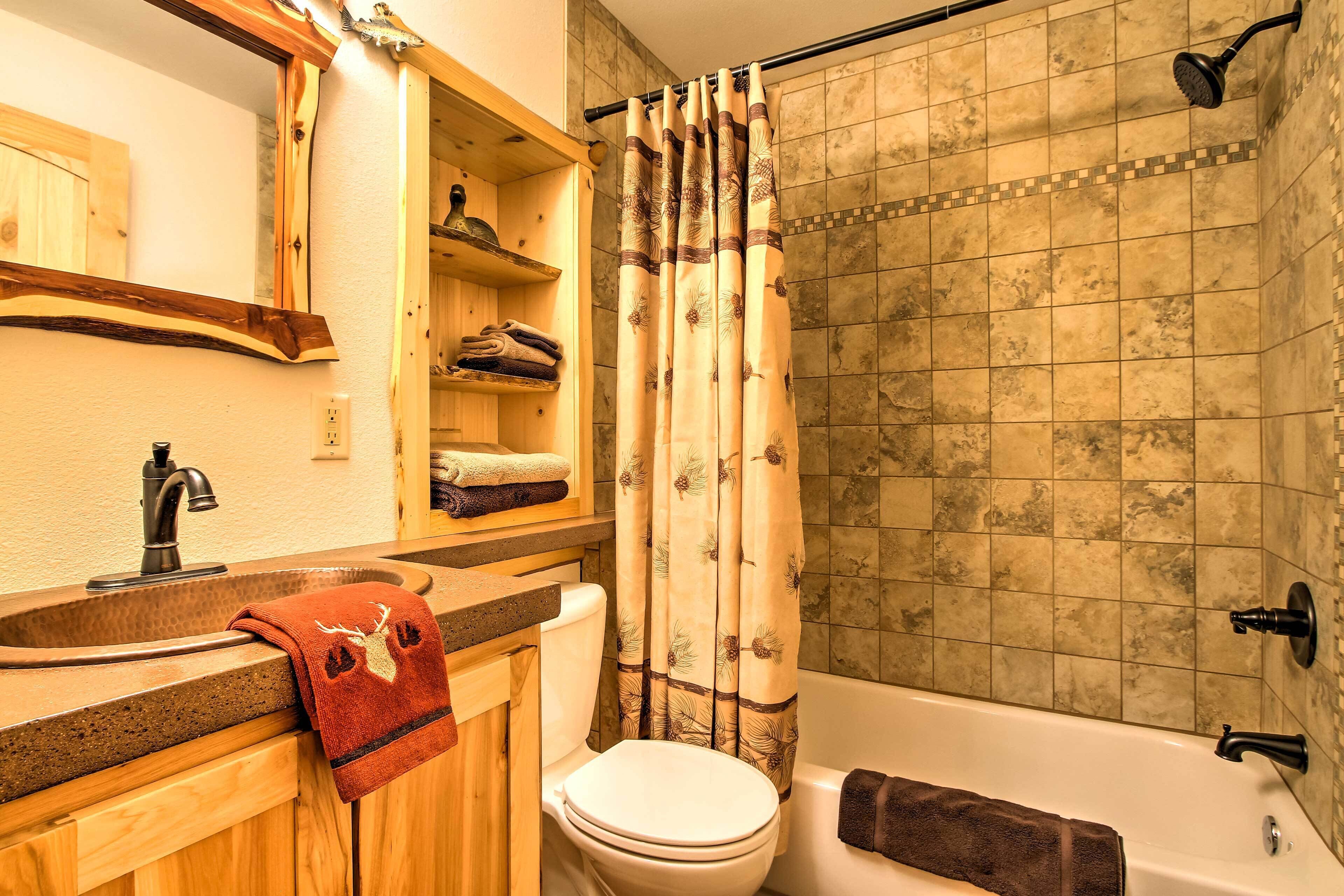 A bathroom with a wooden vanity, a toilet, a bathtub, and a shower curtain with a leaf pattern.