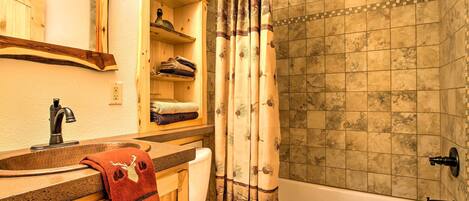 Une salle de bain avec un meuble-lavabo en bois, des toilettes, une baignoire et un rideau de douche orné d’un motif de feuilles.