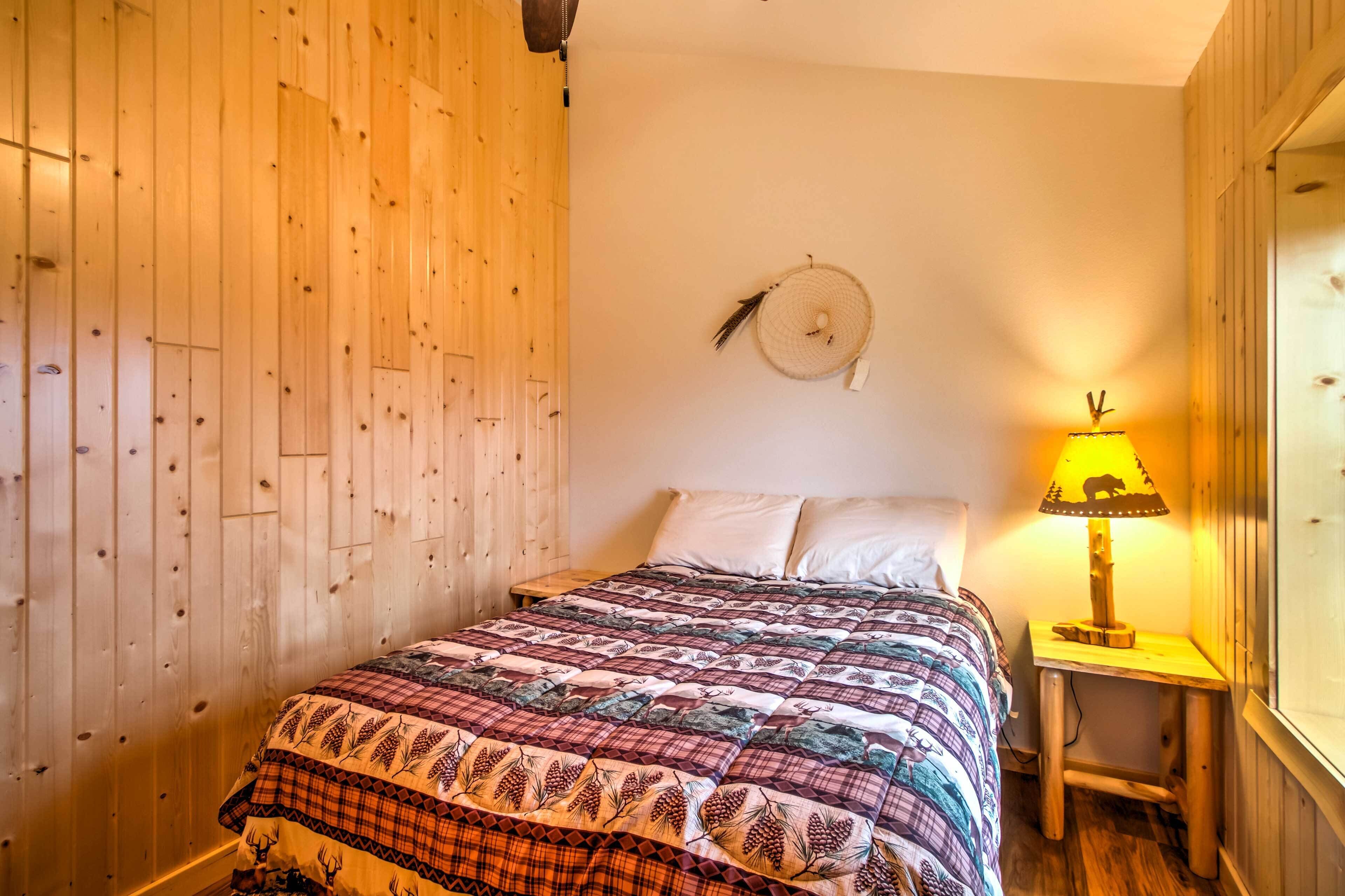 A wooden-paneled room with a bed, a wall-mounted dreamcatcher, and a small table with a lamp.