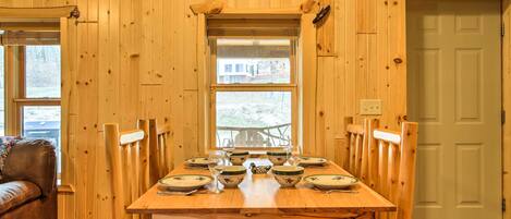 A wooden dining table set for six with chairs, a window above the table, and a door to the right.