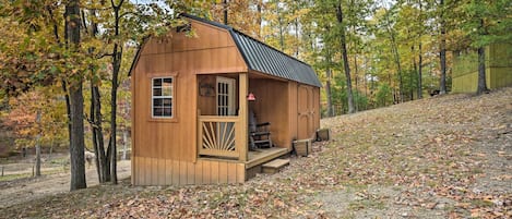 Una pequeña cabaña de madera con un porche, rodeada de árboles con follaje otoñal.