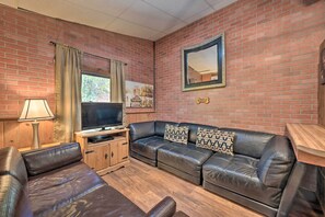 Ein Wohnzimmer mit Backsteinwand, Ledersofa, Holzschrank, Fernseher und Spiegel.