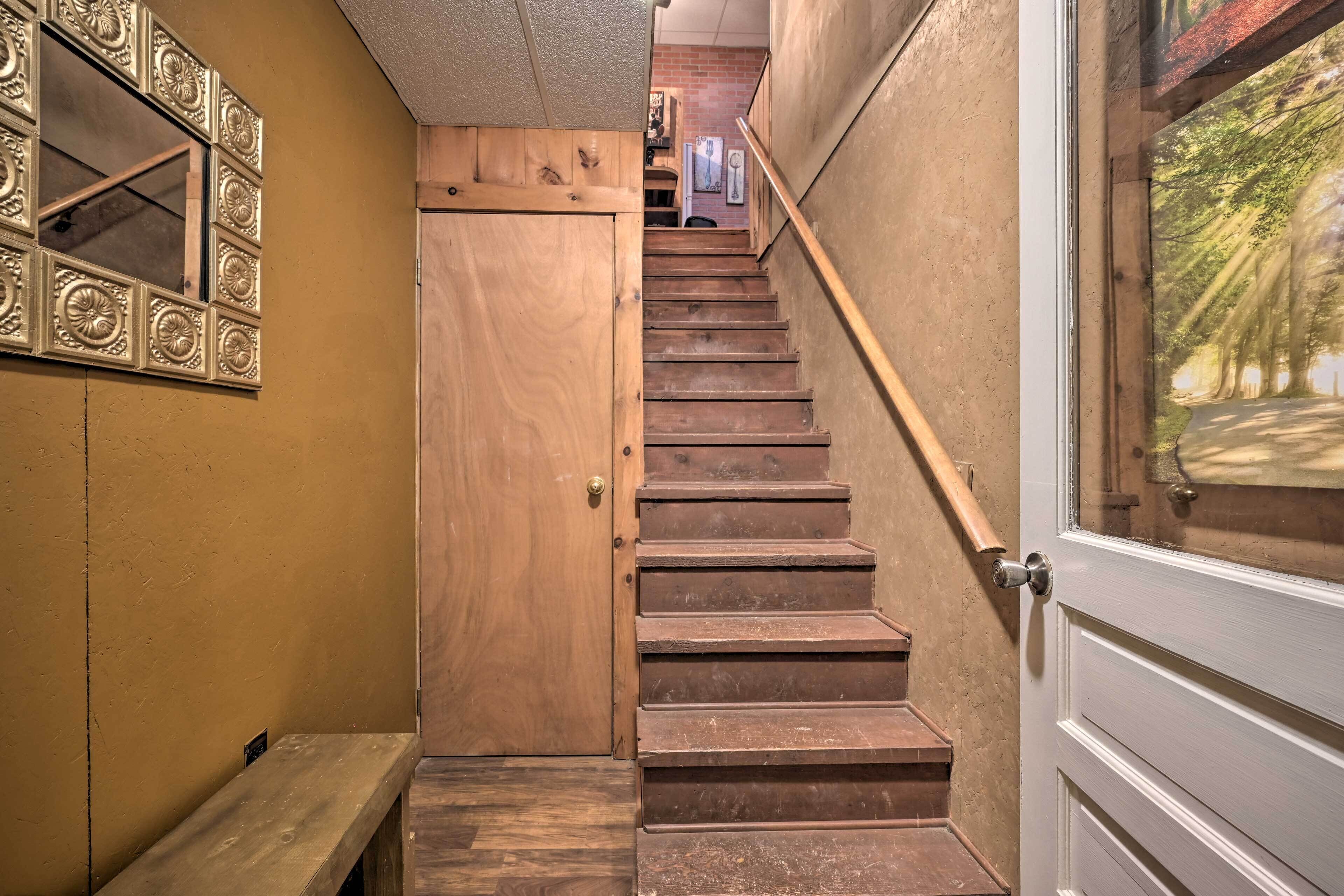 A wooden staircase with a handrail, a door at the top, and a bench at the bottom.