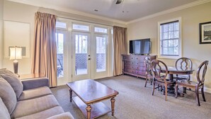 A living room with a sofa, a coffee table, a dining table with chairs, a television on a cabinet, and a ceiling fan. - Anderson Creek Resort Condo on Golf Course w/ Pool (Spring Lake)
