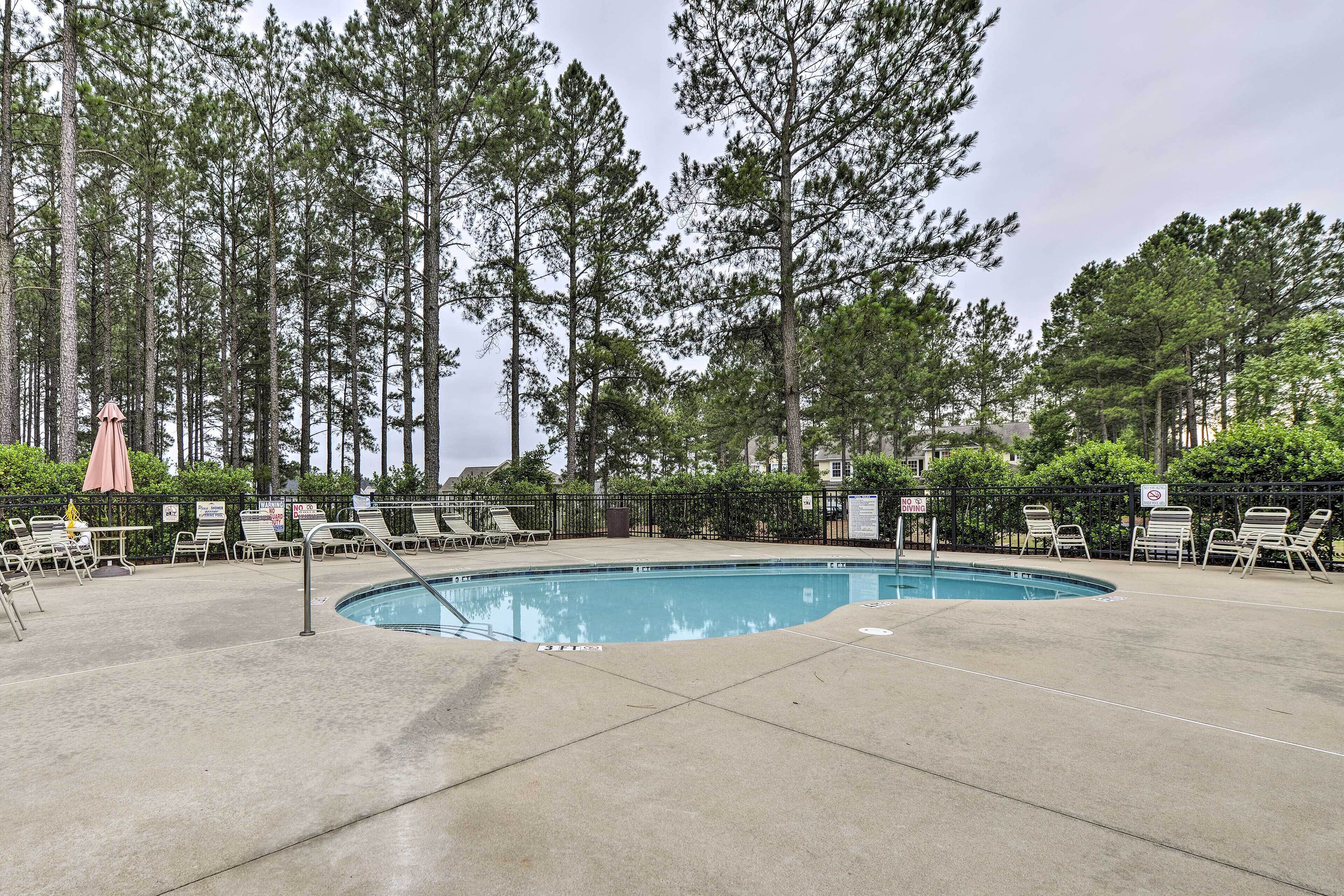 A swimming pool with lounge chairs and umbrellas, surrounded by tall trees.