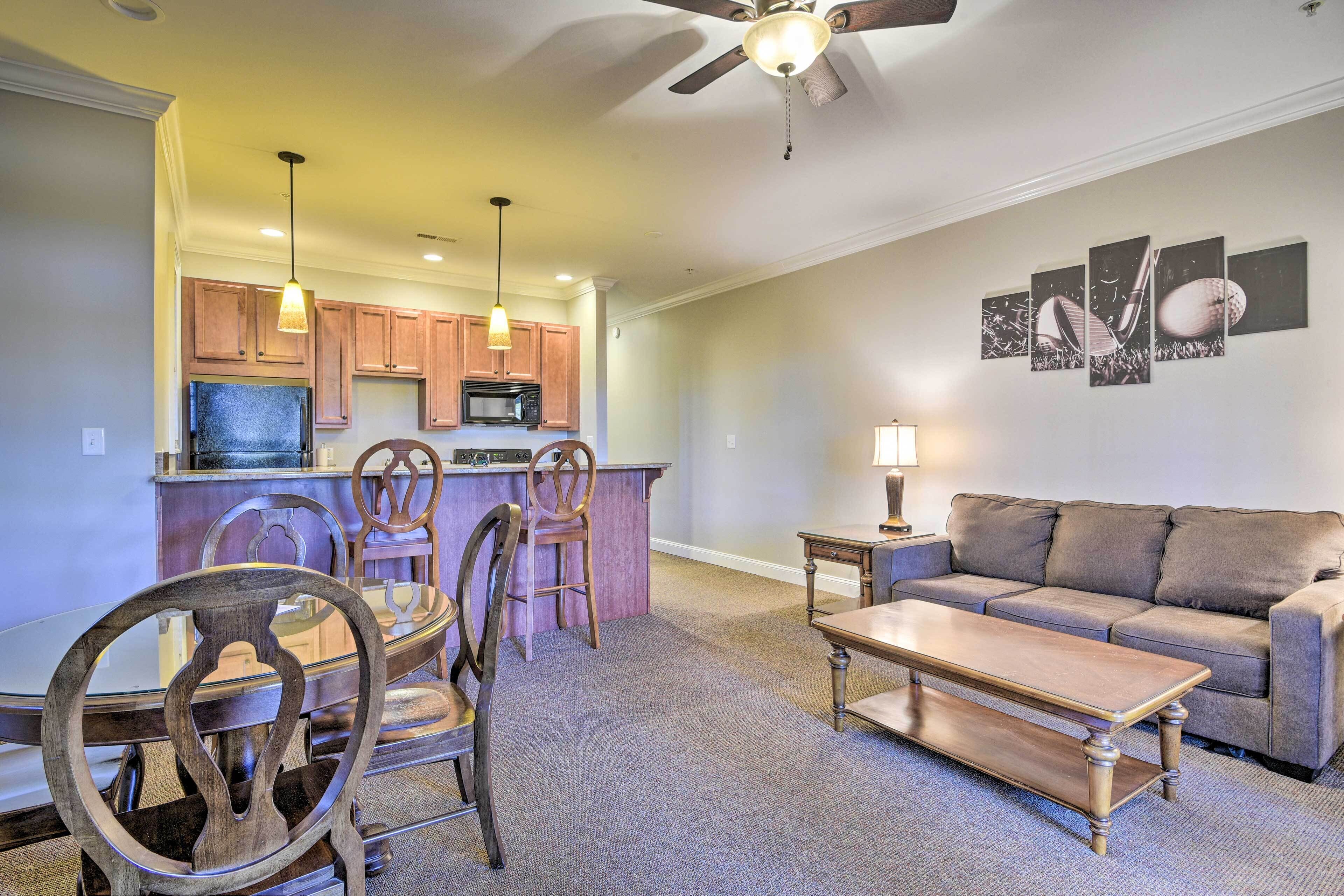 A modern living room with a sofa, coffee table, and dining area with chairs and a small island.