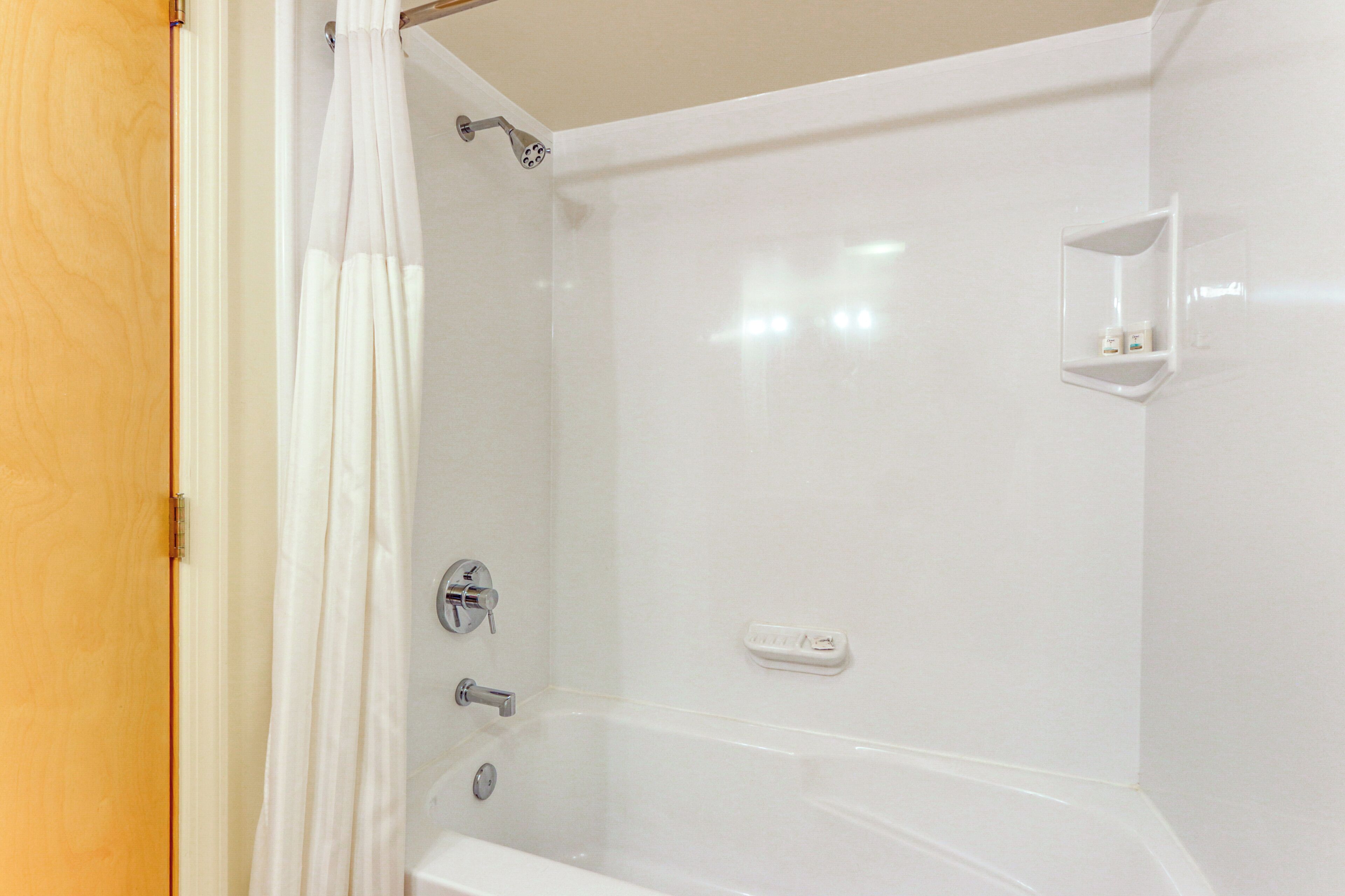 Un baño con bañera, ducha e inodoro. Hay un estante blanco en la pared.