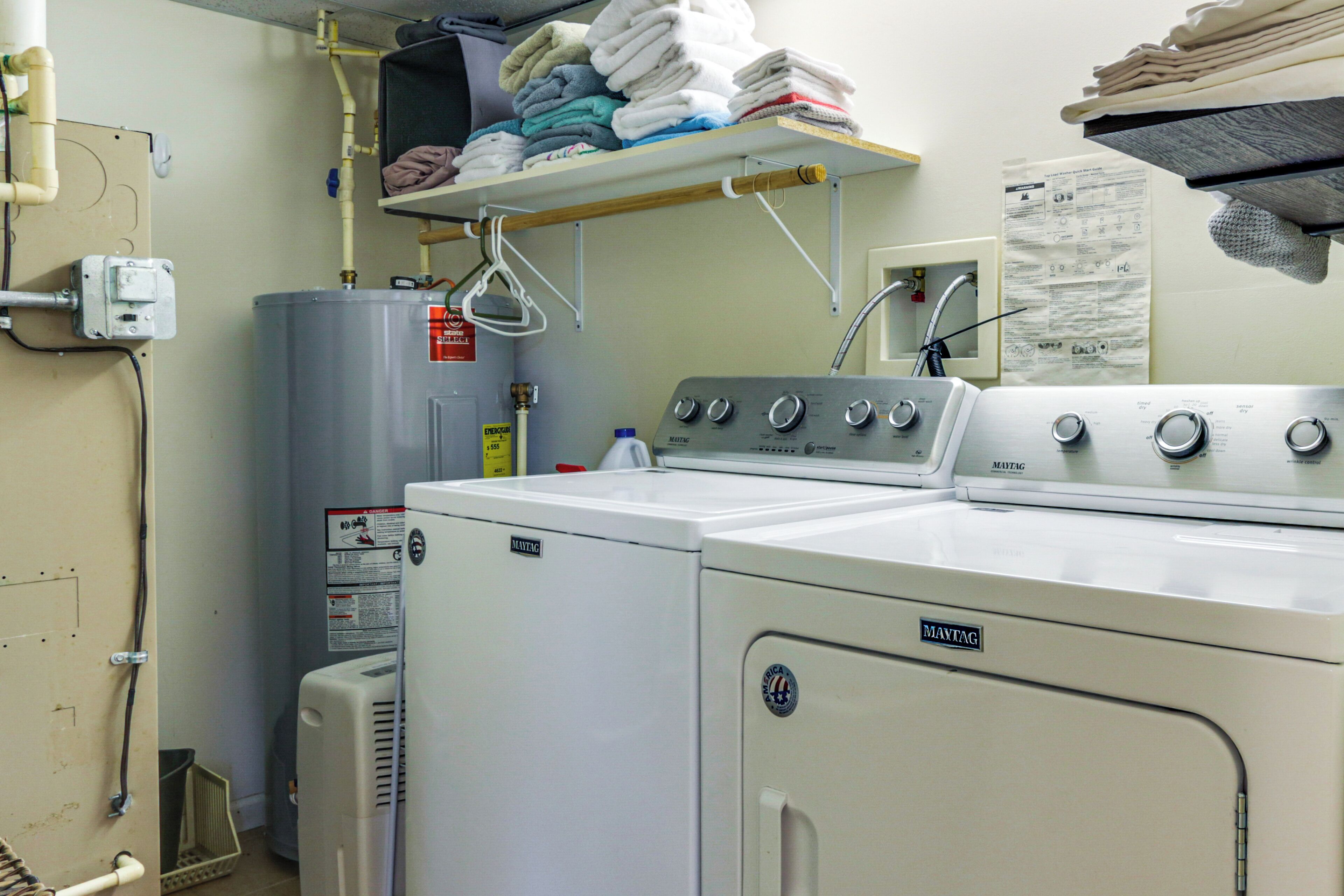 Une buanderie équipée d’un lave-linge et d’un sèche-linge superposés, d’un chauffe-eau et d’étagères où sont pliées les serviettes.