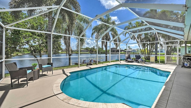 A covered outdoor swimming pool with lounge chairs and a view of a lake. - Dog-friendly Escape w/ Dock & Kayaks in Cape Coral (Cape Coral)