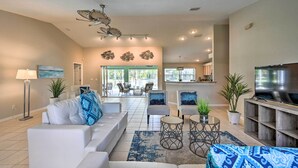 A spacious living room with a white sofa, armchairs, a coffee table, and a TV stand. There is a dining area in the background with a kitchen visible. - Dog-friendly Escape w/ Dock & Kayaks in Cape Coral (Cape Coral)