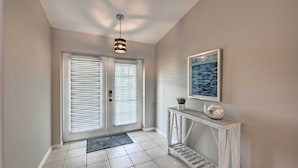 A hallway with a white door, a black and white pendant light, a framed picture on the wall, and a console table with a plant and decorative items. - Dog-friendly Escape w/ Dock & Kayaks in Cape Coral (Cape Coral)