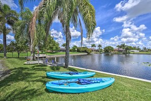 Two kayaks on a grassy area near a lake with palm trees and a dock. - Dog-friendly Escape w/ Dock & Kayaks in Cape Coral (Cape Coral)