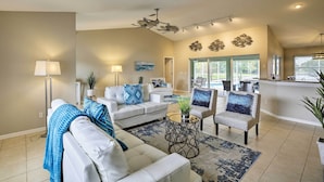 A spacious living room with a white sofa, armchairs, and a coffee table. There is a kitchen area in the background with large windows. - Dog-friendly Escape w/ Dock & Kayaks in Cape Coral (Cape Coral)